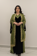 Woman wearing a green embroidered abaya over a black dress against a white background