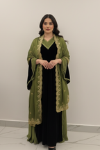 Woman wearing a green embroidered abaya over a black dress against a white background